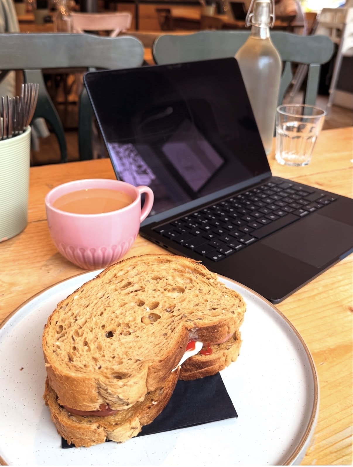 A toasted butty on a plate with a cup of tea and a laptop on a wooden table inside The Green