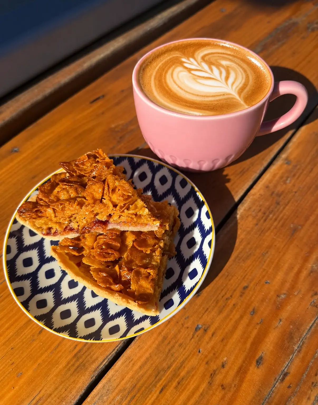 A latte in a pink cup beside a homemade bake
