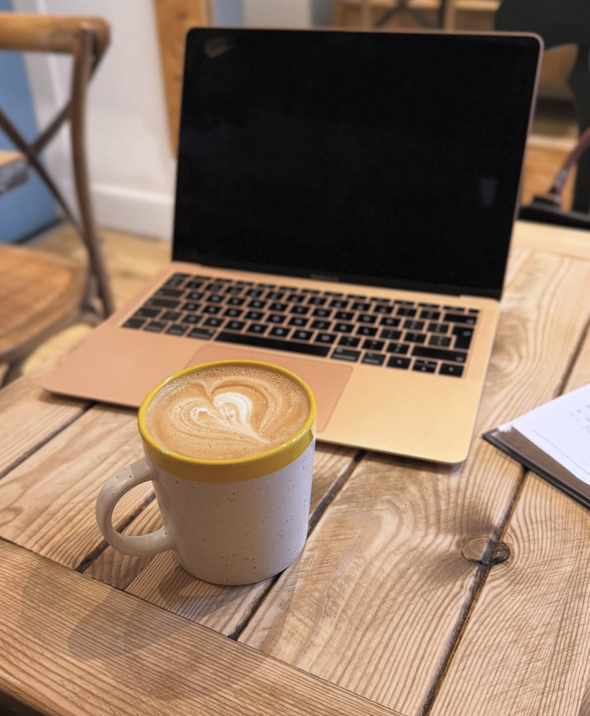 A flat white with latte art in a speckled mug beside a laptop on a wooden table